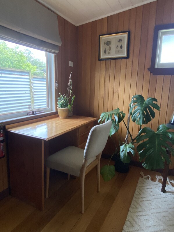 A room with a wooden desk, a chair, a potted plant, and a framed picture on the wall.