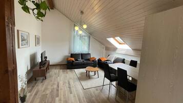 Un appartement moderne de style « loft », doté d’un plafond haut, de planchers en bois, d’un coin repas, d’un salon avec un canapé et des fauteuils, et d’une lucarne.
