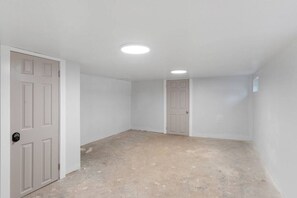 Una habitación con paredes blancas, dos puertas y suelo de hormigón.