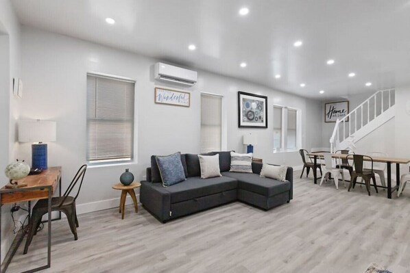 Una sala de estar moderna con un sofá modular, una mesa de comedor con sillas y una escalera.
