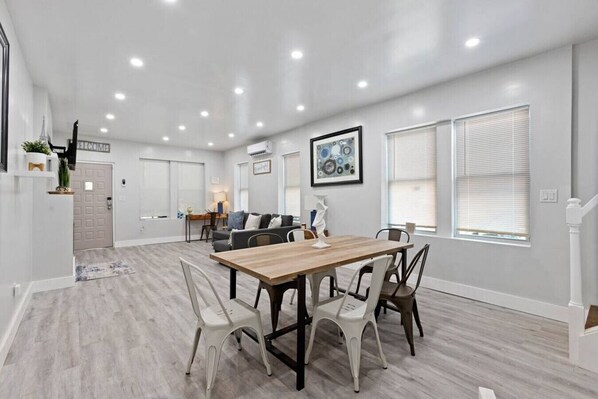 Amplia sala de estar con una mesa y sillas de madera, un sofá y una zona de cocina al fondo.