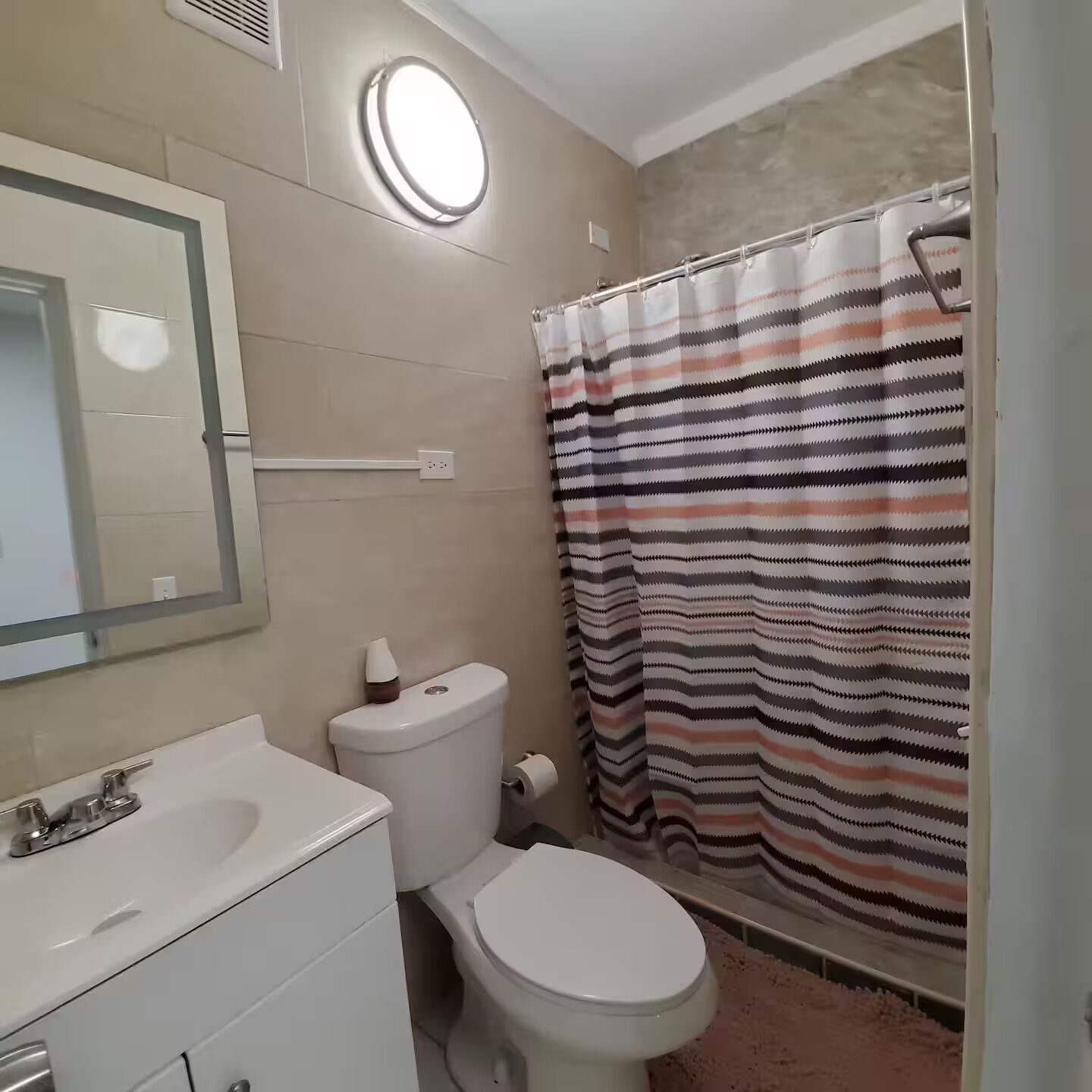 A bathroom with a toilet, sink, mirror, and striped shower curtain.