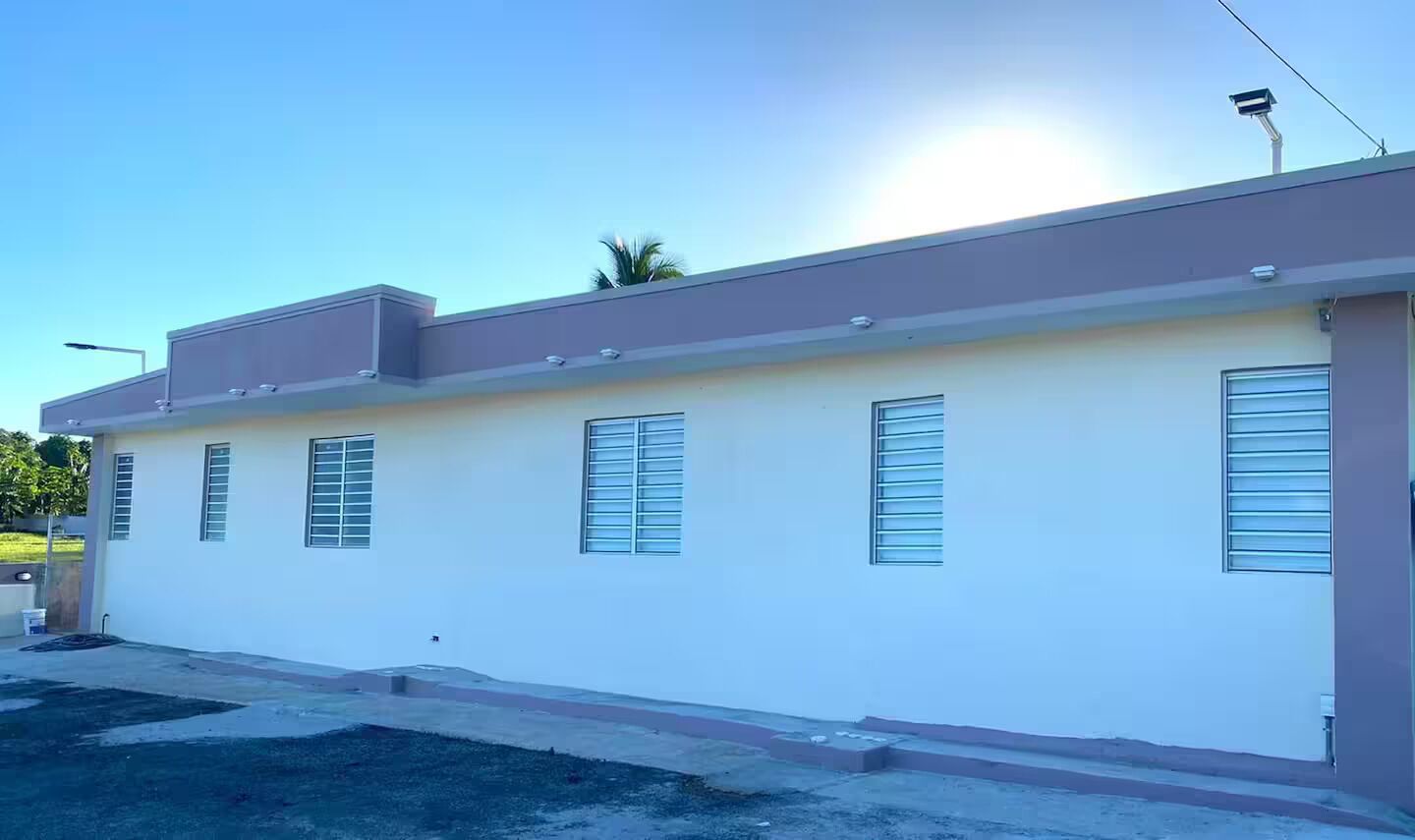 Un bâtiment d’un seul étage, doté d’un toit plat, de nombreuses fenêtres équipées de stores horizontaux et d’une antenne parabolique bien visible.