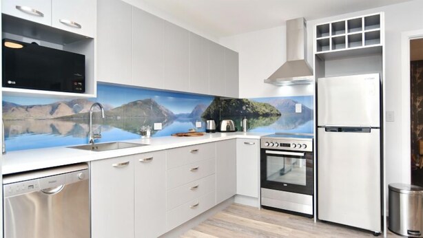 Una cocina moderna con armarios blancos, lavavajillas de acero inoxidable, horno empotrado y refrigerador.