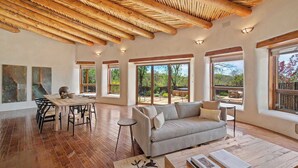 A spacious living area with a wooden ceiling, large windows, a sofa, and a dining table. - Summer Pool, Hot Tub, Stunning Luxury (Santa Fe)