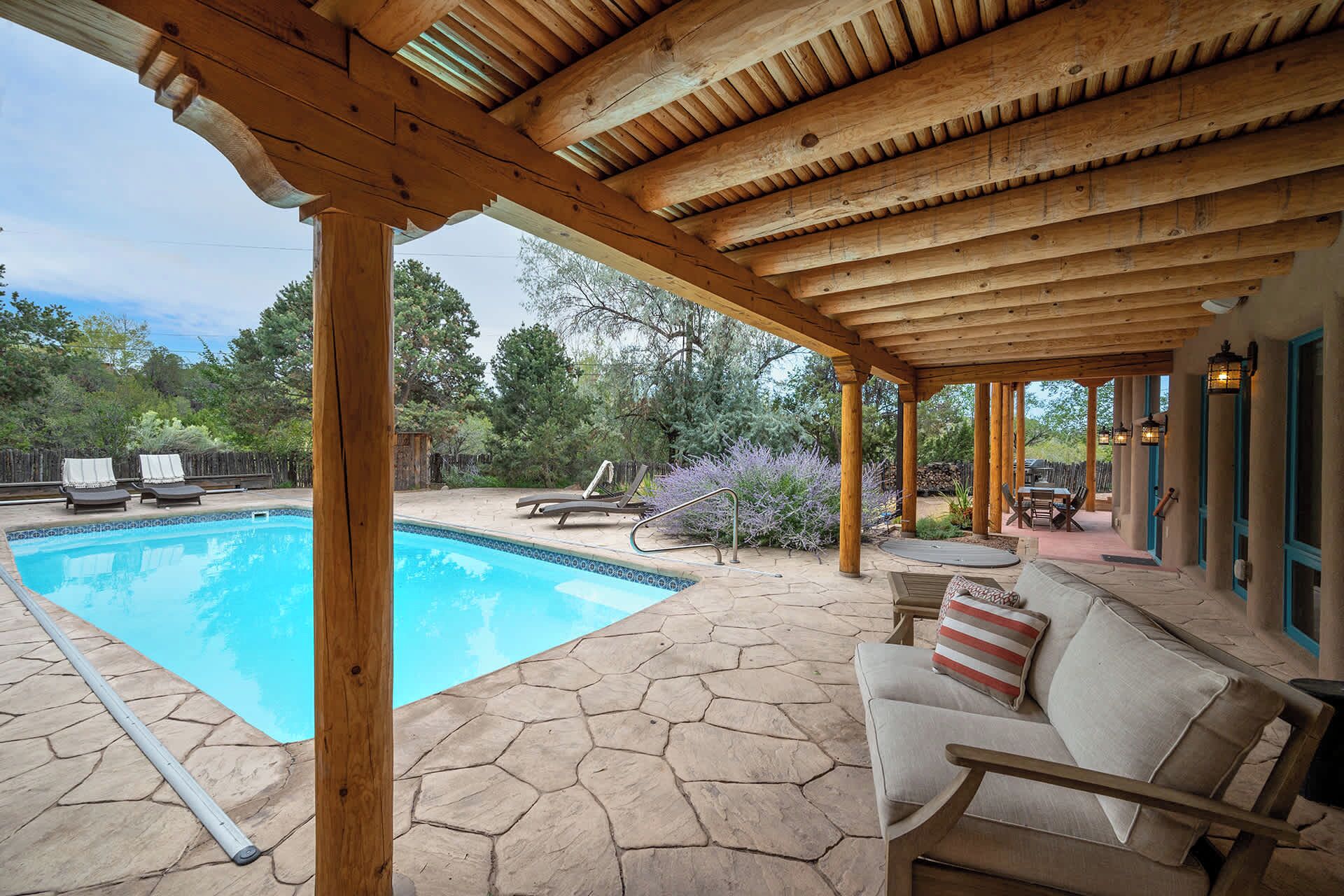A covered outdoor area with a pool, lounge chairs, and a seating area with cushions.