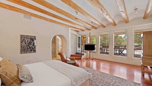 A spacious bedroom with a large bed, wooden beams, a TV, and a view of the outdoors. - Summer Pool, Hot Tub, Stunning Luxury (Santa Fe)
