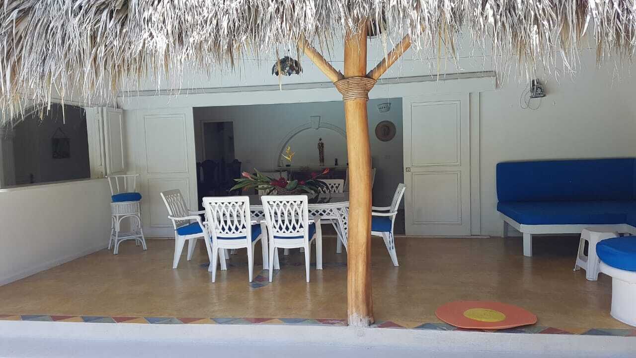 Un coin repas doté d’un toit de chaume, de chaises blanches et d’un canapé bleu.