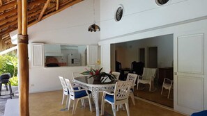 Un'area pranzo con un tavolo rotondo e sedie bianche, una cucina visibile attraverso una porta aperta e una ventola a soffitto.