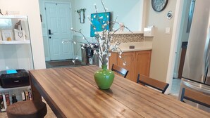Une table de salle à manger en bois, ornée d’un vase vert au centre, et entourée de quatre tabourets.