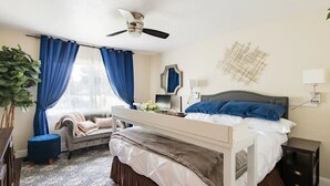 Une chambre à coucher avec un lit, un bureau, une chaise, une plante et un ventilateur de plafond.