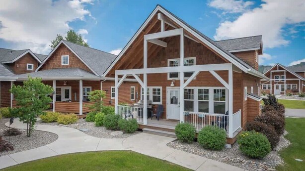 Une maison moderne à deux étages, avec une façade en bois, un porche couvert et un jardin paysager à l’avant.