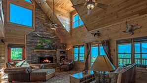 A spacious living room with a stone fireplace, leather furniture, and large windows offering views of the outdoors. - A perfect mountain view getaway (Ellijay)
