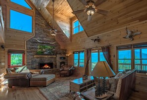 Cozy living area with a stone fireplace, comfortable seating, and large windows offering views of the surrounding landscape.