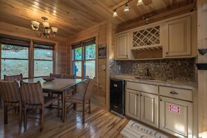 Cozy cabin-style interior with a dining area and kitchen featuring a wooden table, sink, and cabinets.