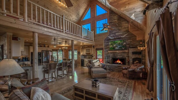 A spacious living area with a stone fireplace, leather furniture, and a high ceiling with wooden beams. - A perfect mountain view getaway (Ellijay)