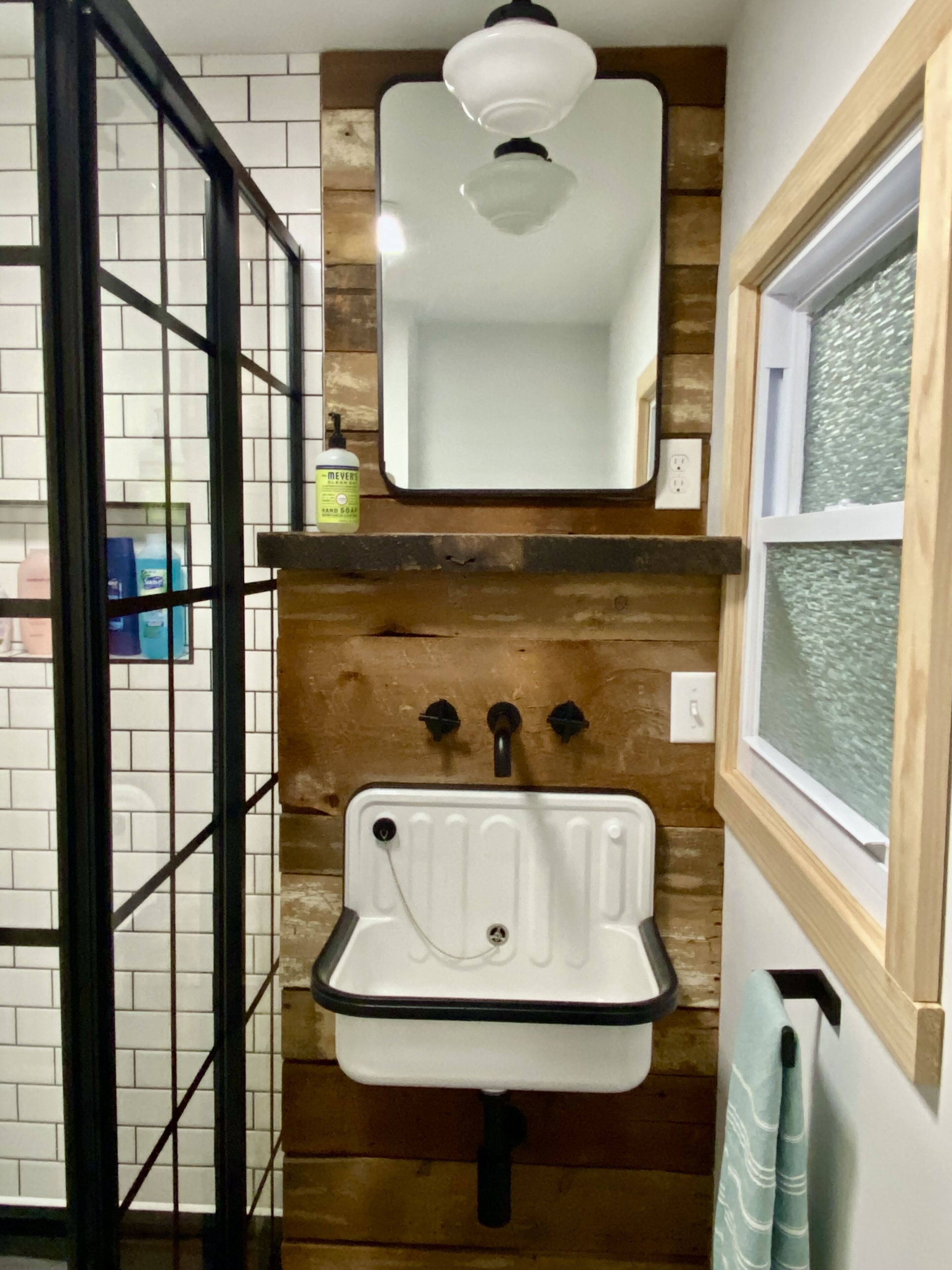 Une salle de bain avec un lavabo blanc, un lambris en bois, un miroir et une fenêtre.
