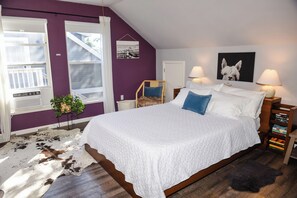 A bedroom with a large bed, two bedside lamps, a mounted picture, a small chair, a potted plant, and a cowhide rug. - Guesthouse in the heart of Historic Folsom (Folsom)