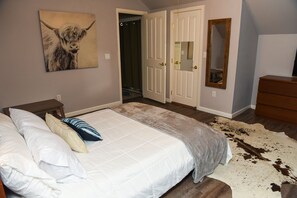 A bedroom with a large bed, a painting of a dog, a mirror, and a wooden dresser.