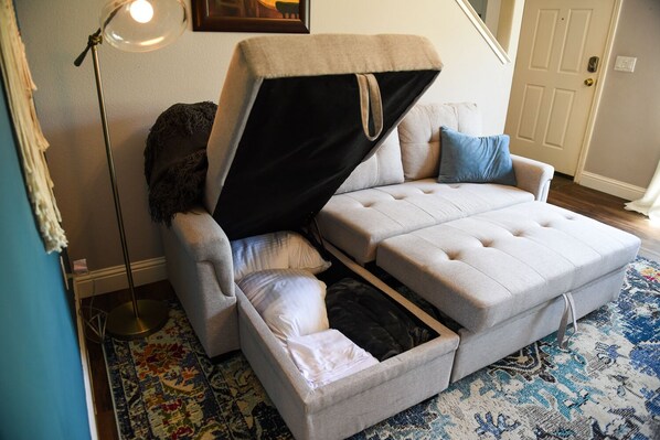 A convertible sofa with a pull-out bed in a room with a patterned rug, a floor lamp, and a door in the background.
