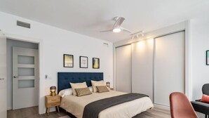 Un dormitorio moderno con una cama grande, un ventilador de techo, un escritorio con silla y un armario.