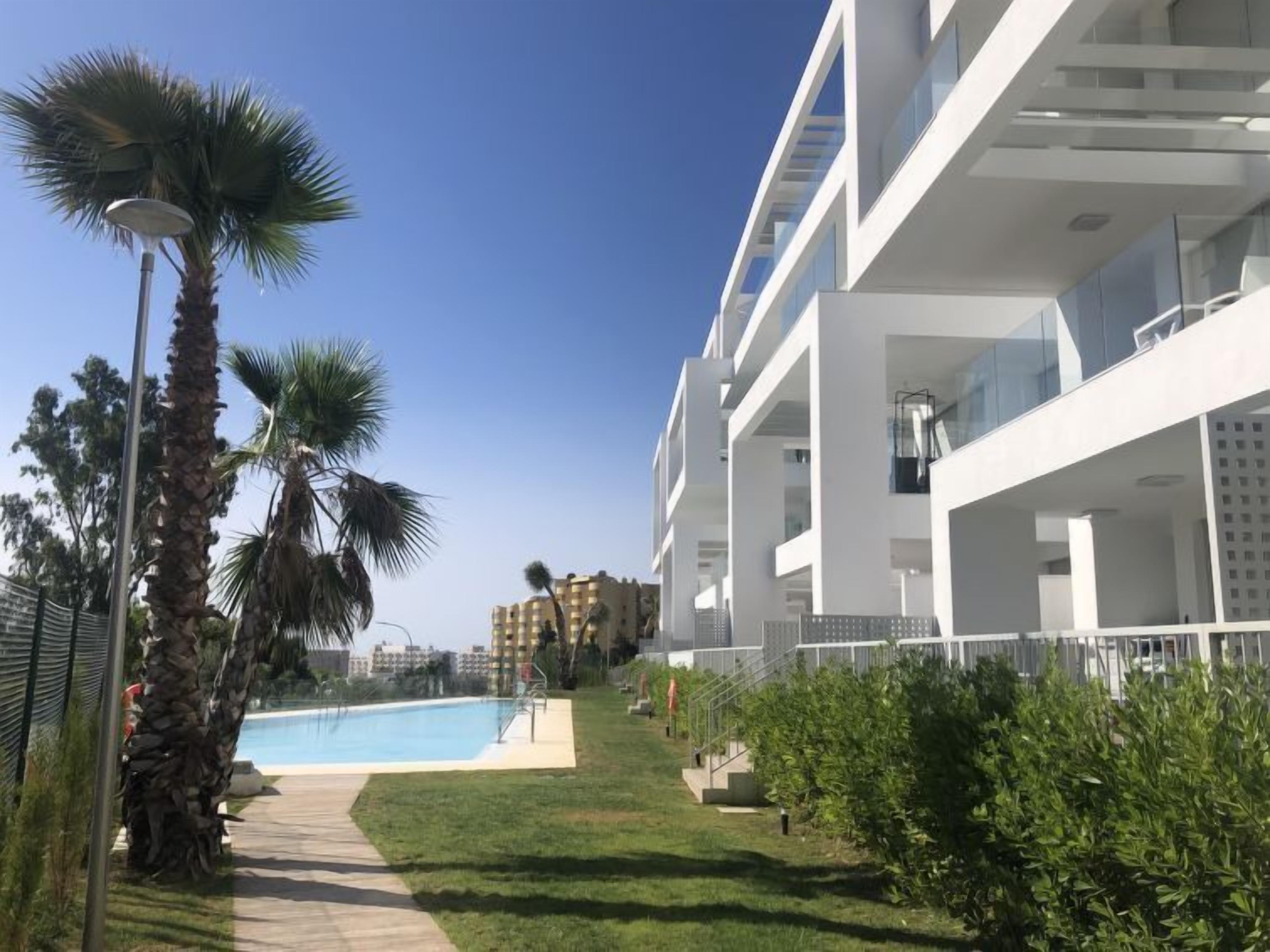 Un edificio moderno con piscina, palmeras y un cielo azul despejado.