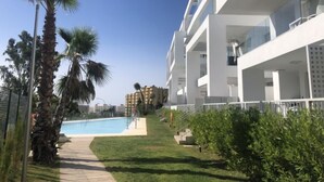 Un edificio moderno con piscina, palmeras y un cielo azul despejado.