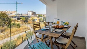 Un balcón con una mesa de madera dispuesta para el desayuno, con vista a una obra en construcción y edificios.