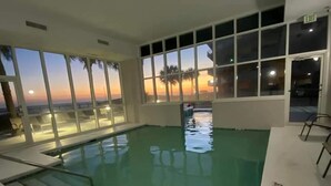 Une piscine intérieure offrant une vue sur le coucher de soleil grâce à de grandes fenêtres.
