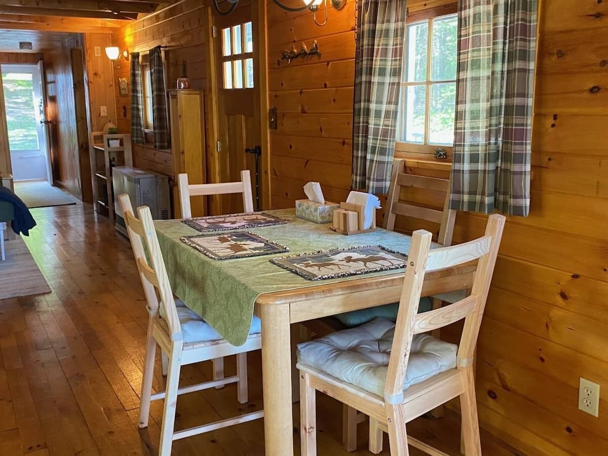 A wooden interior with a dining table set for four, surrounded by wooden chairs with cushioned seats.