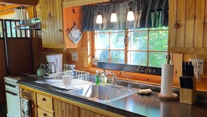 Una cocina con armarios de madera, un lavamanos de acero inoxidable, una estufa y una ventana con cortinas.