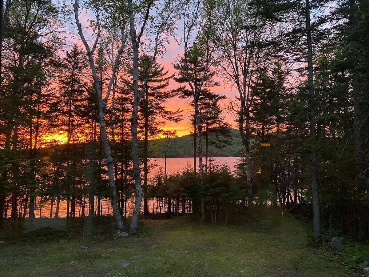 A natural landscape with a lake, surrounded by trees and a clear sky.