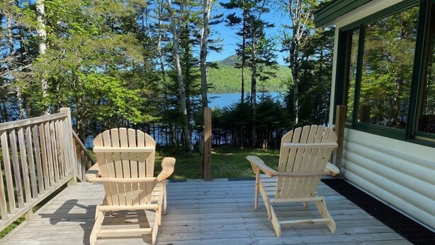 Una terraza de madera con dos sillas Adirondack mirando un lago, rodeado de árboles.