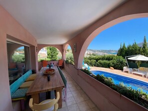A balcony with a wooden table, chairs, and a view of a swimming pool.