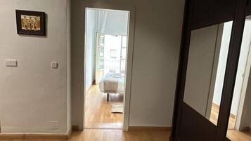 Un pasillo con piso de madera que conduce a un dormitorio con cama y ventana.