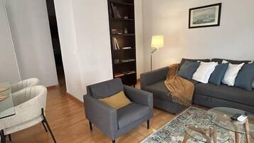 Un soggiorno con un divano grigio, una poltrona, un tavolino in vetro, un tappeto decorato e una libreria.