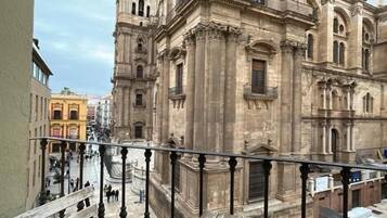 Vista di un edificio storico con architettura classica, caratterizzato da colonne e una torre dell'orologio, ripresa da un balcone con ringhiera in ferro battuto.