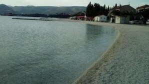 Blick auf die Küste mit ruhiger See, einem Sandstrand und einer Reihe von Gebäuden mit roten Dächern.