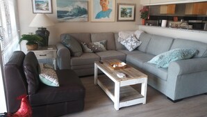 A living room with a sofa, a coffee table, and a decorative rooster. There are framed pictures on the wall and a plant on the side table.
