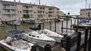 A marina with several boats docked, wooden pilings, and a row of multi-story buildings with balconies.