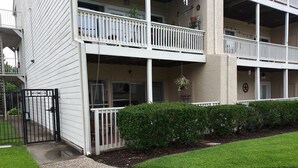 A two-story building with a white exterior, a gated entrance, and a small porch area with potted plants.