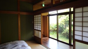 A traditional Japanese room with tatami flooring, a bed, sliding shoji doors, and a view of greenery outside.