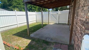 A covered patio area with a brick wall and a white fence in the background. - 1/1 Guesthouse 6mi from Beach for Perfect Getaway (Fort Walton Beach)