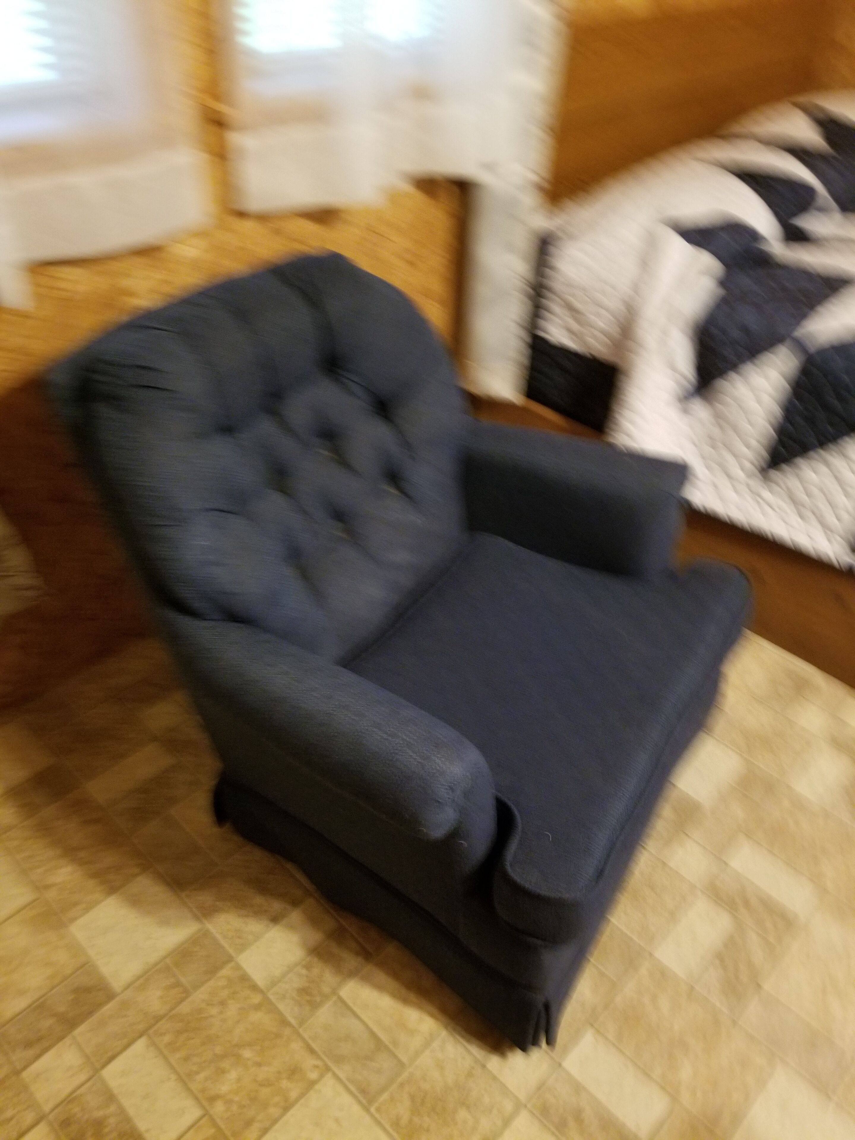 A dark blue armchair with a tufted backrest and armrests, placed on a patterned floor.