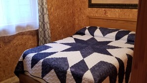 Una habitación con pared de madera texturizada, una cama con colcha estampada de estrellas, una ventana con cortina decorada y un cuadro con caballos en la pared.
