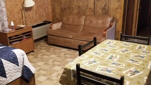 Una habitación acogedora con un sofá de cuero marrón, una mesa de madera con mantel estampado, un mueble de madera pequeño y un televisor montado en la pared.