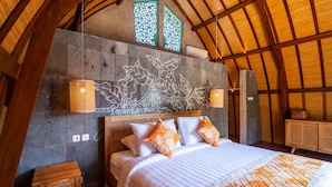 A bedroom with a stone wall, a wooden ceiling, and a bed with white and orange bedding. - Sunset Paradise Nusa Dua (Nusa Dua)