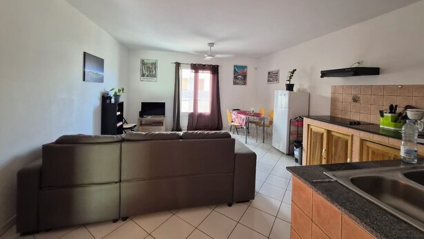 A living room with a sofa, a dining area with a table and chairs, a kitchen with cabinets and a sink, and a ceiling fan. - T2 Escale sudiste, south of Reunion Island (Saint-Louis)