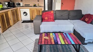A compact living space with a sofa, a colorful coffee table, a washing machine, and a kitchenette. - T2 Escale sudiste, south of Reunion Island (Saint-Louis)