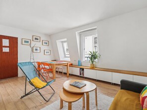 A modern living room with a dining area, a wooden floor, a window with a view, and a plant on the windowsill. - Nice apartment in the heart of Paris by Weekome (Paris)